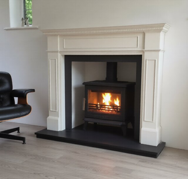 A wood burning stove in a plain painted fireboard chamber with a restored timber fireplace