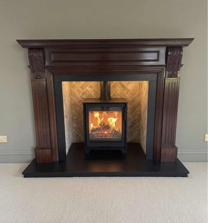 A timber fireplace surround with a black granite hearth and a herringbone brick chamber, fitted by Carl Finnell