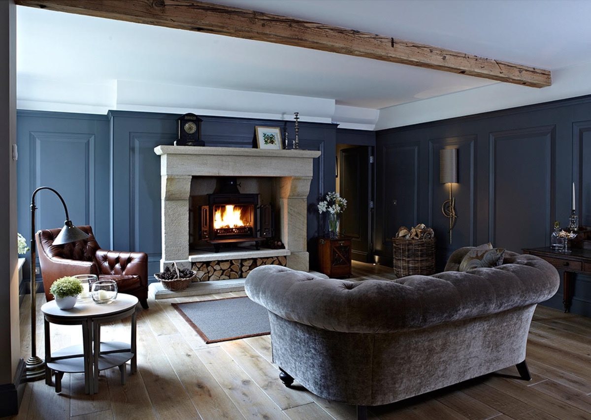 A natural stone fireplace built into a panelled living room with an oak beam and a wood burning stove